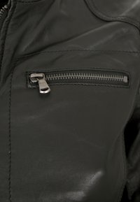 Schwarze Lederjacke mit einer Reißverschlusstasche auf der Brust, metallischem Reißverschluss, strukturiertem Finish und sichtbaren Nähdetails.