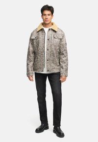 Denimjakke med en tekstureret grå overflade, beige fleecekrave, trykknapper, to forlommer, parret med sorte jeans og sorte Støvler.