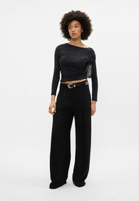 Melna garām piedurknēm topi ar smalku ziedu rakstu, apvienots ar augsto jostasvietu platām melnām biksēm un teksturētu melnu rokassomu.