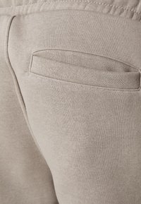Beige sweatpants fabric with soft texture, featuring a single welt pocket on the back. Elastic waistband at the top.