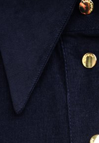 Granatowa koszula z kordurowego materiału z wywijanym kołnierzykiem i złotymi guzikami. Tkanina ma teksturowany, prążkowany wzór.