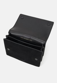 Czarny skórzany portfel z wykończeniem zamszowym, posiadający dwie przegródki, zatrzaski oraz tłoczone logo w środku.