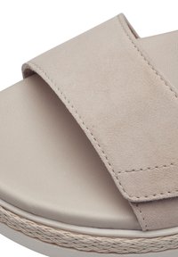 Beige mokkasandaali leveällä hihnalla, pehmeällä pohjalla, punottu pohja ja sileä pinta; minimaalinen muotoilu, jossa on ommeltuja yksityiskohtia.