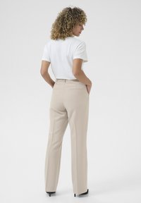 Beige maßgeschneiderte Hosen mit geradem Schnitt, strukturiertem Stoff, zwei Gesäßtaschen und einem glatten Bund. Getragen mit einem weißen T-Shirt.