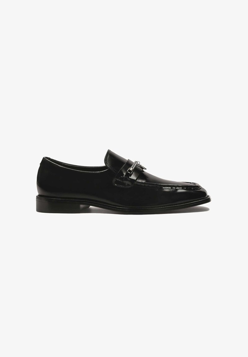 Mustad nahast loafers ümarate varvastega, läikiva viimistlusega ja dekoratiivse hõbedast pandlaga rihmal. Madal kergelt laotud konts ja sile tekstuur.