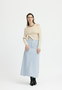 Beige, schulterfreier, gerippter Pullover, kombiniert mit einem blau-weißen, gestreiften langen Rock mit einem Schlitz vorne, abgerundet mit schwarzen spitzen Schuhen.