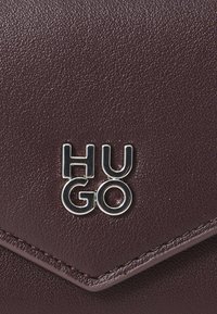 Bordeaux lederen portemonnee met een gestructureerde afwerking, voorzien van een metalen "HUGO" logo. Het ontwerp heeft een diagonale klep-sluiting.