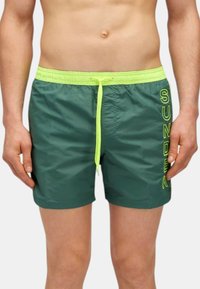 Pantaloni da bagno verdi realizzati in materiale leggero con un cordino giallo neon e la scritta ricamata "SUNDEK" sul lato. Presentano un elastico in vita.