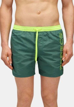 Pantaloni da bagno verdi realizzati in materiale leggero con un cordino giallo neon e la scritta ricamata "SUNDEK" sul lato. Presentano un elastico in vita.