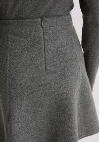 Gros plan sur une personne portant une jupe en laine gris foncé avec une fermeture éclair visible dans le dos et un haut à manches longues assorti de couleur gris foncé.