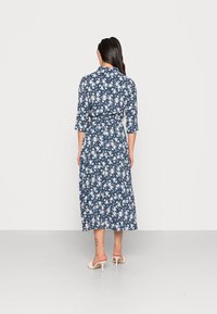 Mörkblå blommig klänning med bindning i midjan, trekvartsärmar och längd till mitt på vaden, med vita blommönster över hela.