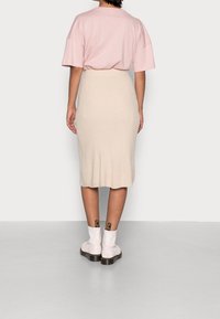 Světle růžové oversized tričko spárované s béžovou žebrovanou sukní do délky kolen a lesklými bílými kotníkovými botami s černými kovovými detaily.