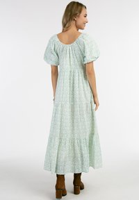Maxi kjole i lys grøn med blomstermønster, korte puffærmer, elastisk ryg og lagdelt nederdel. Bæret med brune hælede støvler.