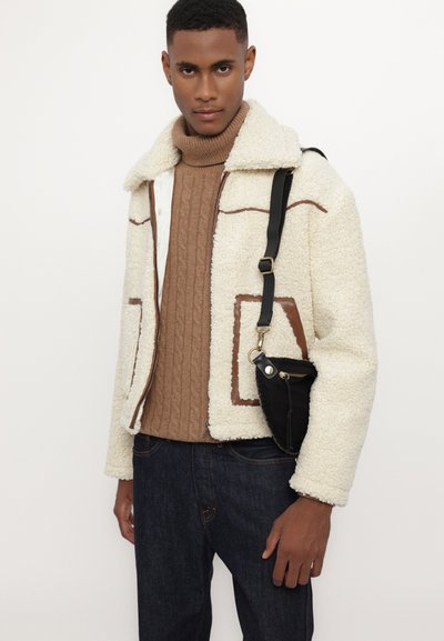 Cream faux shearling jacket with brown faux leather accents, zippered front, large patch pockets, and a black bag with a strap.