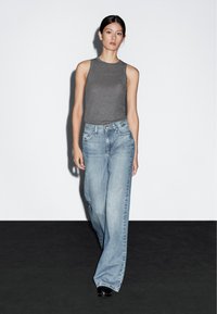 Grå ärmlös topp, ljusblå vid jeans med blekt tvätt, och svart skor. Enkel design utan distinkta mönster eller metallbeslag.