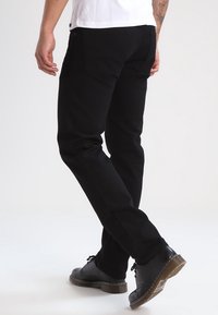 Pantalones de algodón negros con un corte recto, que incluyen bolsillos traseros y una textura suave, combinados con zapatos de cuero negros.