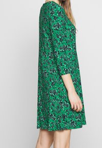 Green floral dress with three-quarter sleeves, featuring a loose fit, soft material, and a vibrant pattern of navy flowers on a green background.