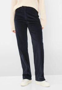 Pantaloni in corduroy blu navale con design a gamba dritta, dotati di chiusura con bottone e tasche laterali, abbinati a sneakers bianche.