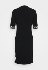 Robe noire longueur genou avec manches courtes, présentant des bandes blanches avec un texte noir audacieux sur les manches et les coutures latérales.