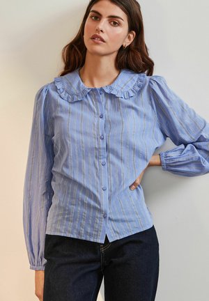 Blouse bleu clair à manches longues avec des rayures, col froncé et manches bouffantes. Le tissu semble lisse avec un léger éclat et une texture subtile.