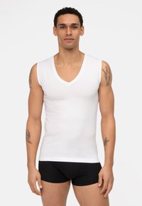 Witte katoenen mouwloze V-hals t-shirt, met een gladde textuur, fitted ontwerp, gedragen met zwarte shorts, met zichtbaar armtattoo's.