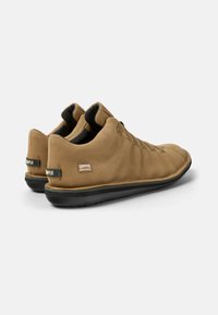 Sneaker in suede marrone elegante, con una forma curva, suola in gomma nera e un design dei lacci minimalista. Presenta dettagli a marchio sul tallone.