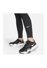 Zwarte sportieve schoenen met een bovenwerk van mesh, wit Nike-logo en witte zool, gecombineerd met zwarte legging met een klein wit logo.