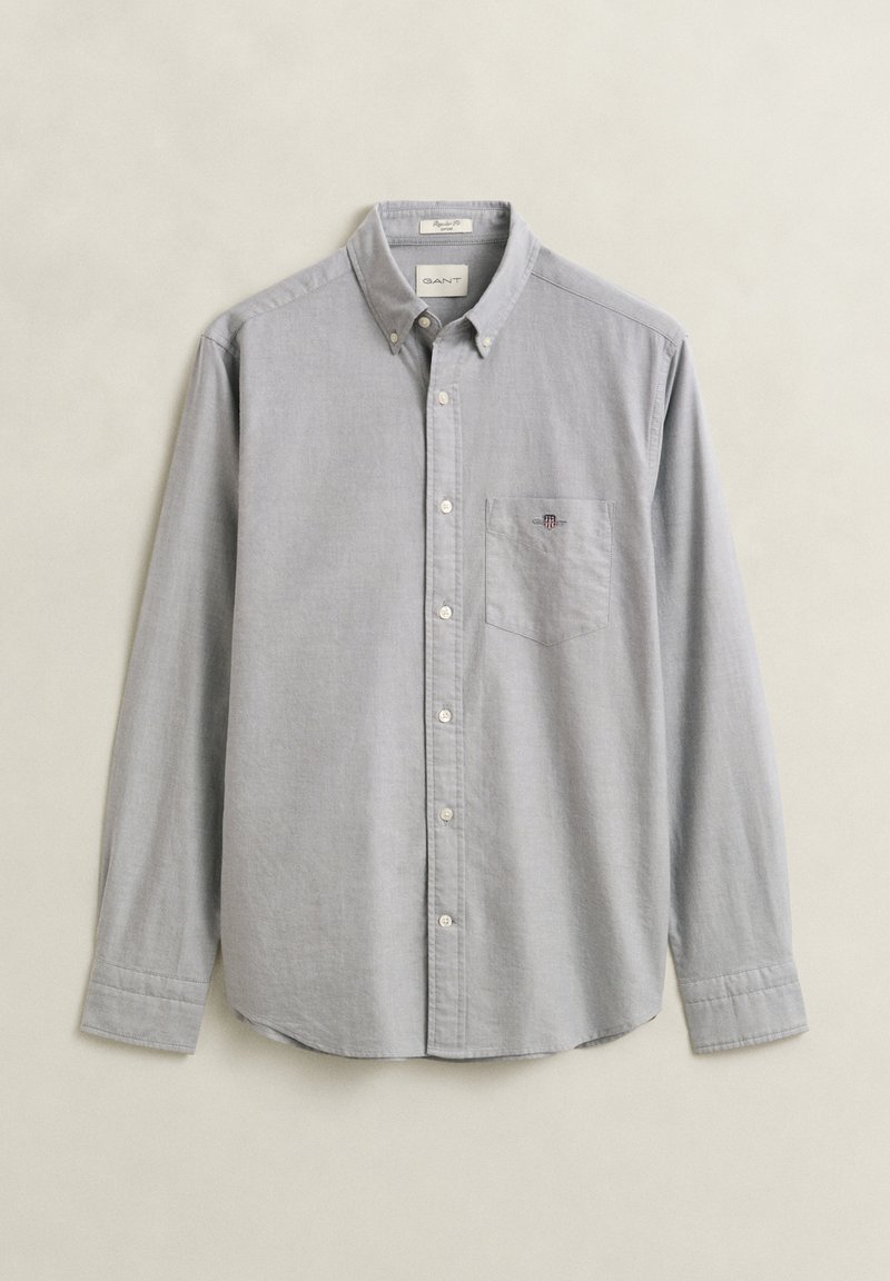 Chemise gris clair boutonnée, manches longues, poche avant avec petit logo et col boutonné sur fond uni.