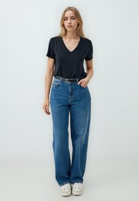T-shirt nera con scollatura a V abbinata a jeans in denim blu larghi. I jeans presentano una vita alta e un design a cinque tasche, accentuato da una cintura nera.