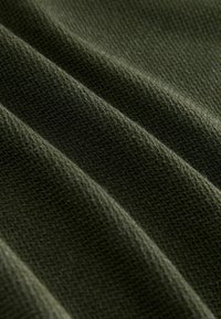 Texturiertes grünes Gewebe mit fester Strickweise, das auffällige diagonale Falten und eine einheitliche Oberfläche aufweist, wodurch seine Weichheit und Dicke betont wird.