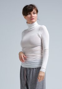 Hvid langærmet turtleneck-trøje, lavet af et tyndt, let materiale. Glat tekstur, tætsiddende design, parret med grå afslappede bukser.