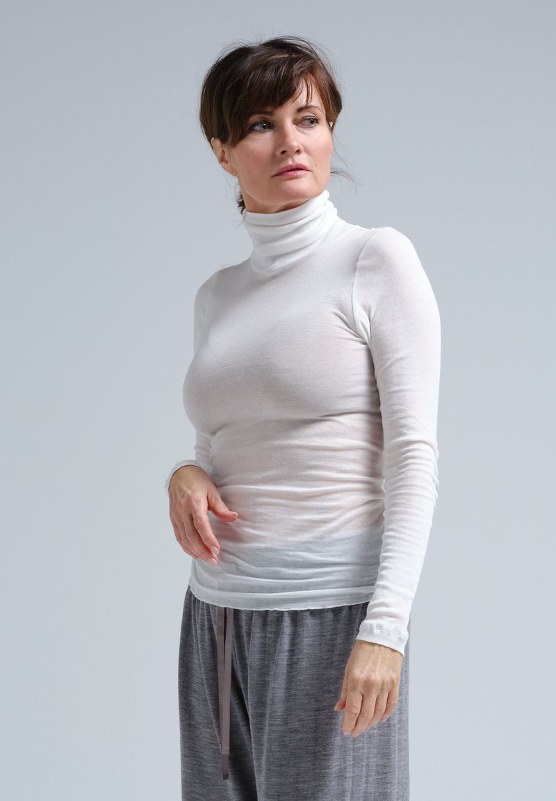 Weiße Langarm-Turtleneck-Bluse, aus einem dünnen, leichten Stoff gefertigt. Glatte Textur, figurbetontes Design, kombiniert mit grauen lässigen Hosen.