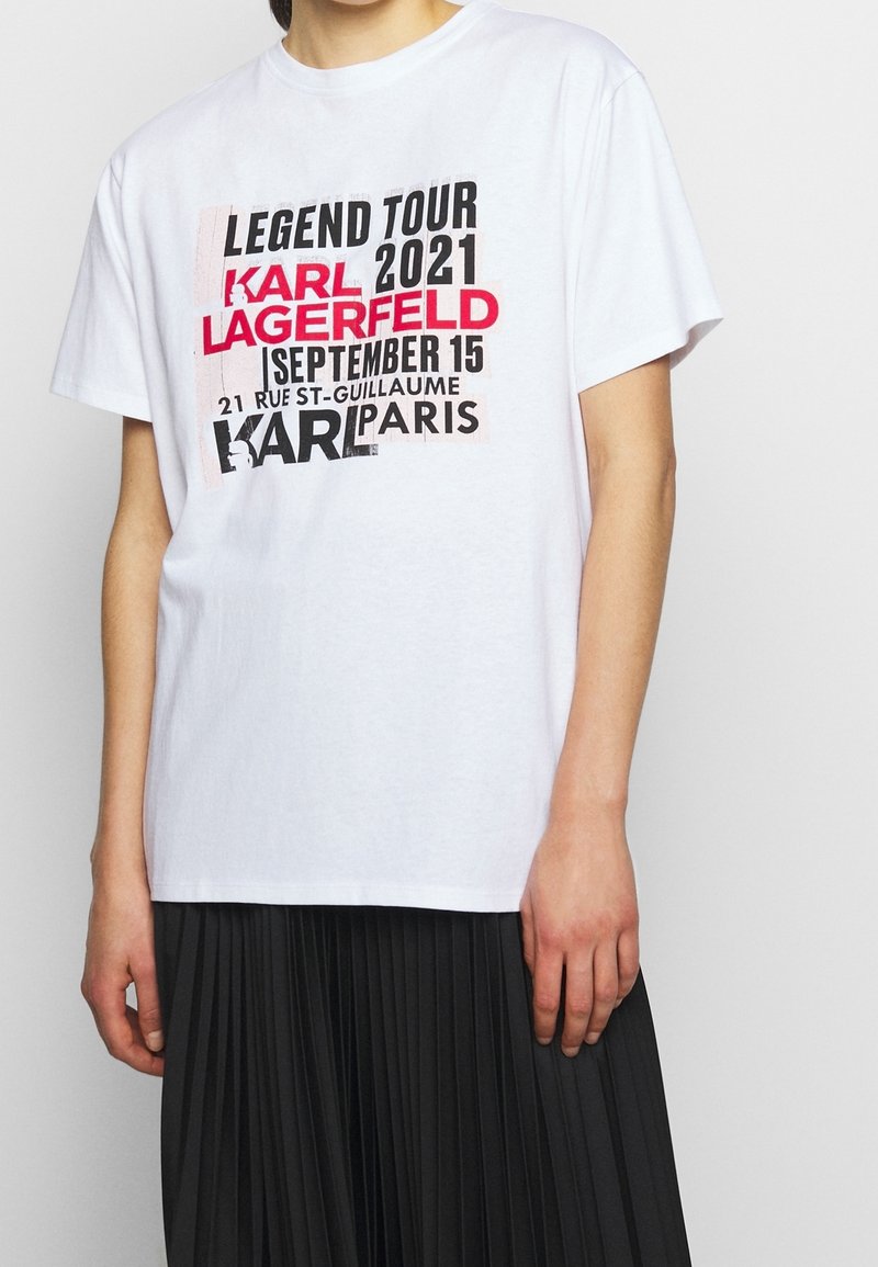 Bílý bavlněný tričko s grafickým potiskem a černým a červeným textem. Potisky zahrnují "Legend Tour", "Karl Lagerfeld" a detaily o Paříži.