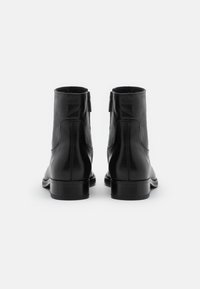 Bottes cheville en cuir noir à finition lisse, bout arrondi, fermeture éclair latérale et petit talon empilé. Design classique pour un port polyvalent.