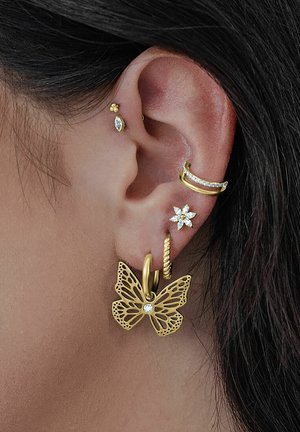 Gold butterfly-shaped earring with intricate cutouts and clear crystal accent. Several additional gold studs and hoops adorn the ear.