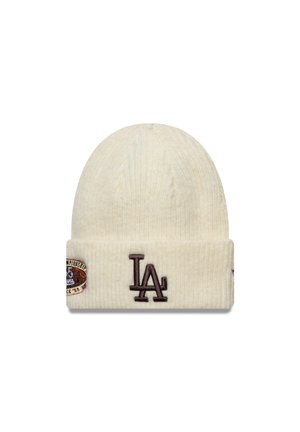 Crèmekleurige gebreide muts met geribbelde textuur, met een bruin "LA"-logo en een ronde patch met tekst en graphics aan de voorkant.