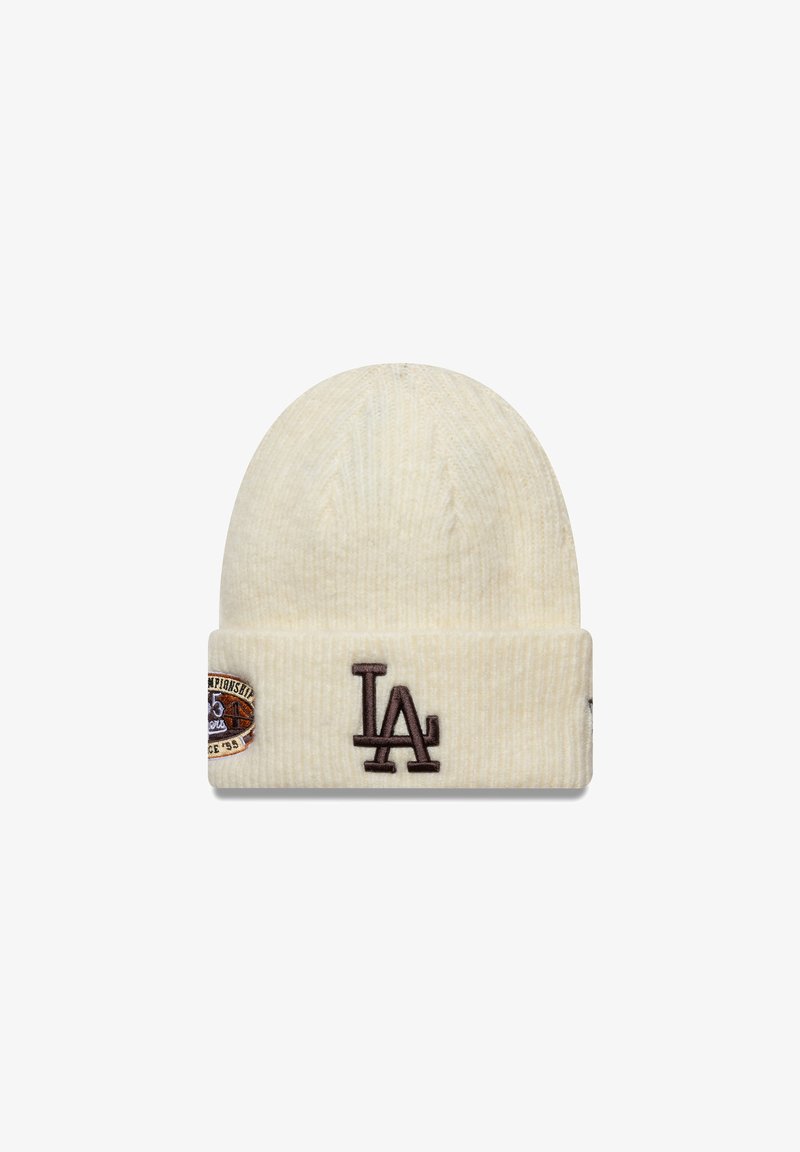 Krémová pletená čepice s ribbovanou texturou, která na přední straně obsahuje hnědé logo "LA" a kulatou nášivku s textem a grafikou.