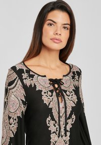 Top negro con bordado floral y paisley en tonos de rosa y crema, que presenta un escote en V con un detalle de cordones.