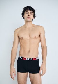 Black boxer briefs with a red and white "DIESEL" logo waistband, made of soft fabric. The design features a form-fitting cut.