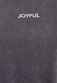 Tumši pelēka kokvilnas t-krekls ar baltu izšūtu tekstu "JOYFUL". Gluda tekstūra bez redzamām rakstiem vai rotājumiem.