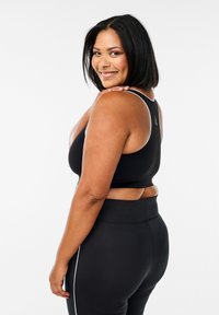 Reggiseno sportivo nero con design a racerback, caratterizzato da un accento bianco lungo le spalline. Abbinato a leggings neri a vita alta con strisce laterali.