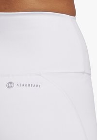 Białe legginsy sportowe o wysokim stanie z elastycznym pasem i szarym logo "AEROREADY". Gładka tkanina z minimalnymi detalami szwów.