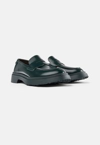 Grüne Lederloafers mit glatter Oberfläche, die über einen erhöhten Riemen an der Vorderseite und eine strukturierte schwarze Gummisohle verfügen.