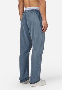 Ανοιχτό μπλε φόρμα με χαλαρή εφαρμογή, ελαστική μέση και πλαϊνές ραφές. Συνδυασμένο με λευκά αθλητικά παπούτσια. Μαλακό, υφασμάτινο ύφασμα με υφή.