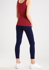 Punainen ja tummansininen raidallinen hihaton paita yhdistettynä yksivärisiin tummansinisiin legginsseihin ja valkoisiin lenkkareihin. Kapeat lahkeet, joissa on sileä pinta ja tiukka siluetti.