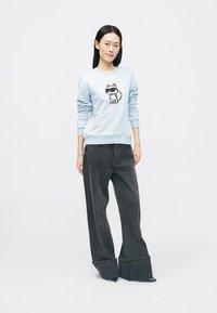 Sweatshirt azul claro com um gráfico de um cão em estilo de cartoon. Combinado com jeans de perna larga, cinza escuro, apresentando um design de bainha dobrada único.