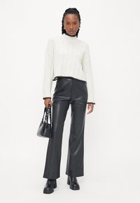 Cropped, cream knit sweater with a high collar and black accents, paired with black leather flared pants and chunky black heeled boots.