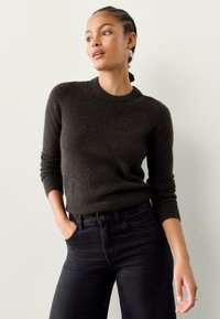 Donkergroene gebreide trui met een ronde hals en geribde manchetten, gedragen met hoge taille zwarte jeans. Gladde textuur en aangesloten ontwerp.