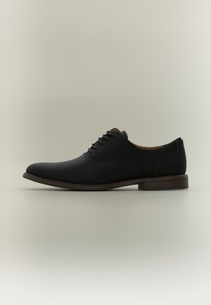 Chaussure habillée pour homme en cuir noir avec lacets, petit talon et bout arrondi lisse, vue de profil sur fond neutre.
