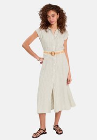 Robe chemise vert clair à rayures blanches verticales, manches courtes et longueur genou. Accentuée par une ceinture tressée beige et des sandales.
